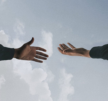 Two hands reach towards each other, with a backdrop of a blue sky with clouds