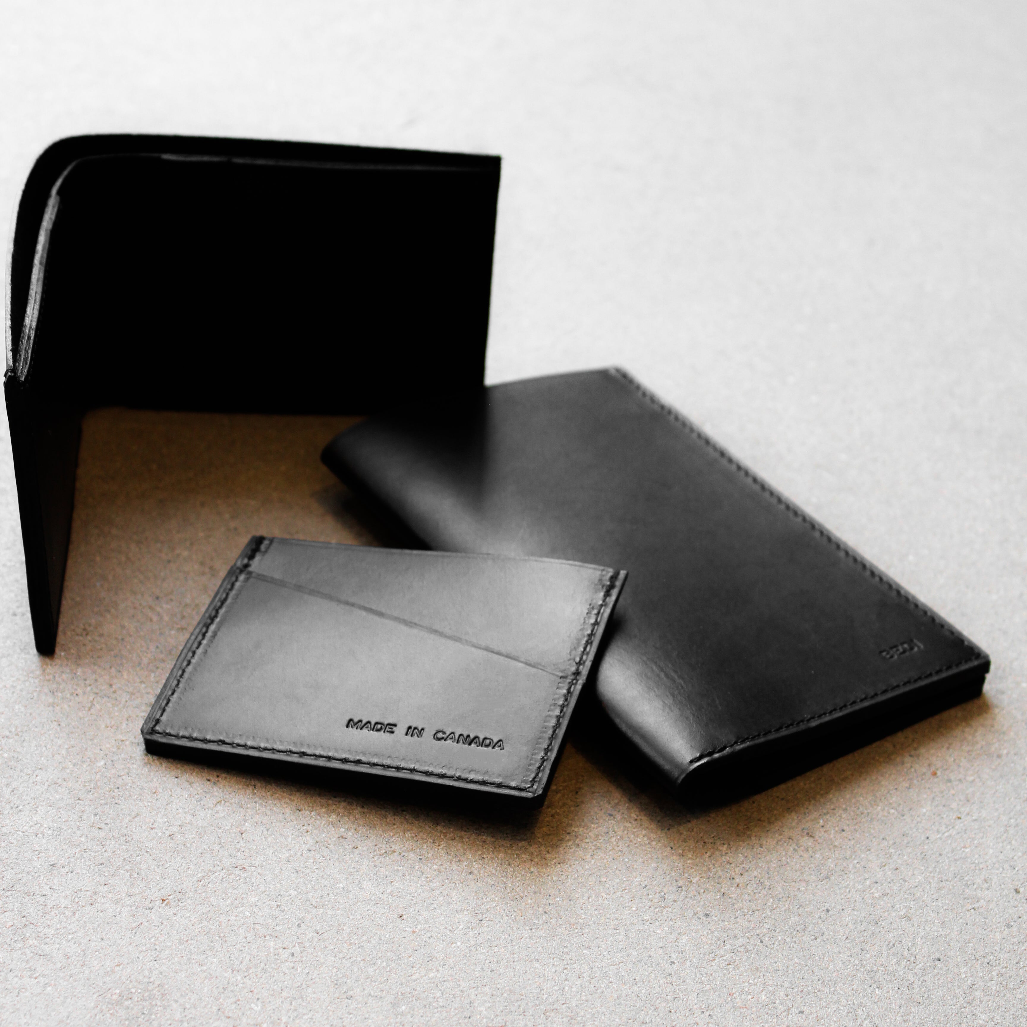 Group of three black leather wallets on a textured grey surface