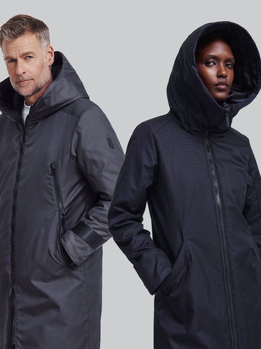 A male and a female model both wearing winter coats pose against a plain background