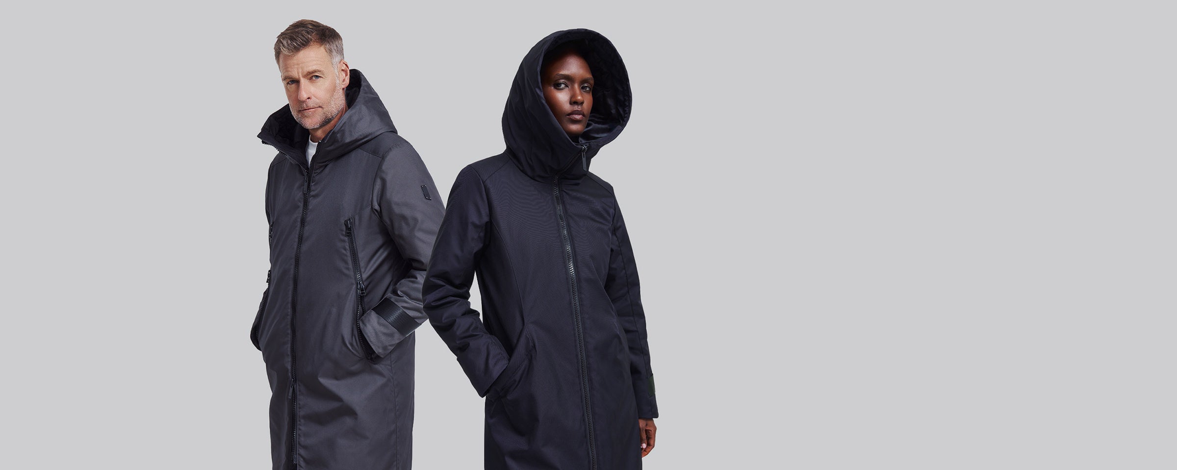 A male and a female model both wearing winter coats pose against a plain background