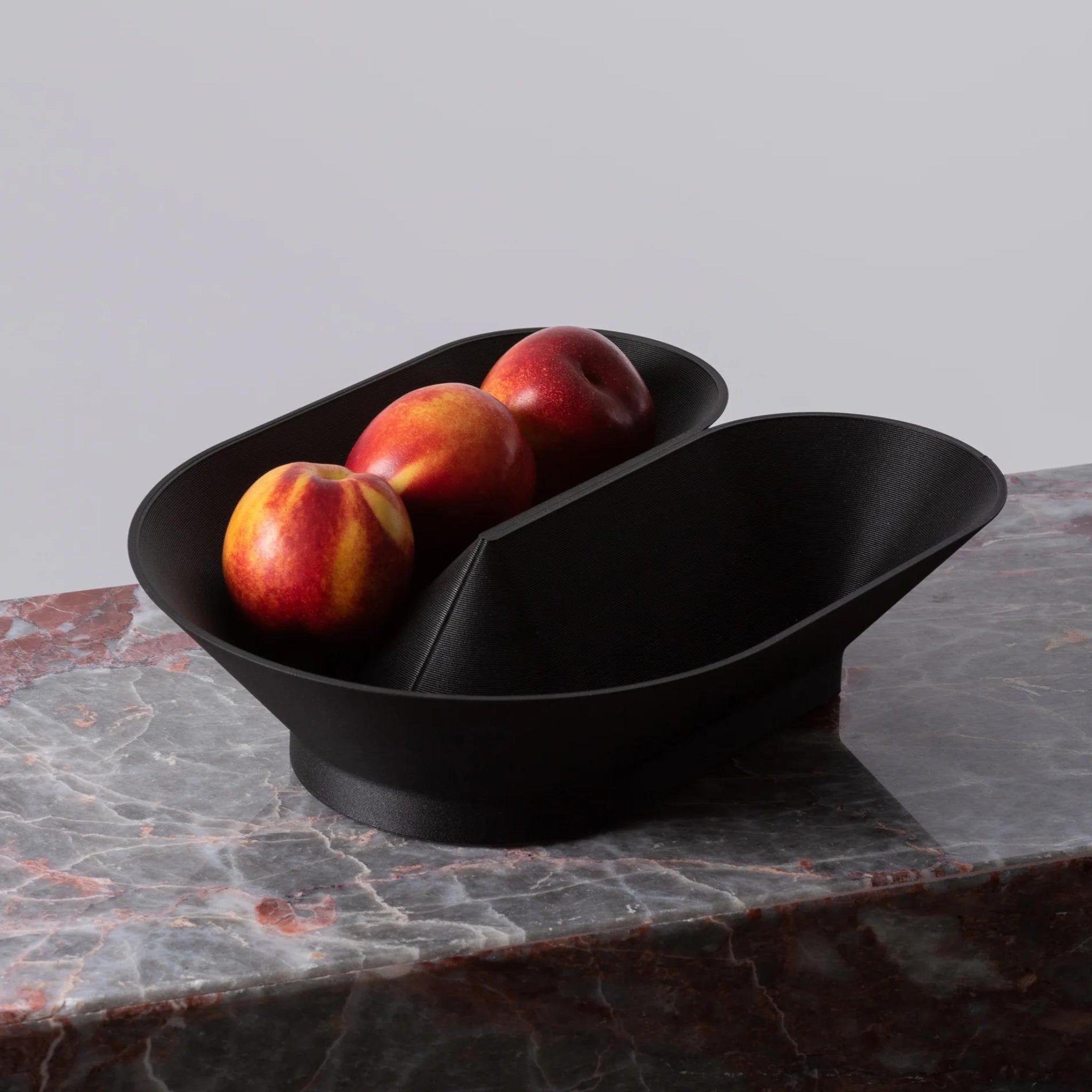 Cyrc U fruit bowl in black. 3D printed recycled plastic bowl holding peaches on a marble surface. 