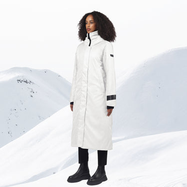 A woman standing in a long white winter coat with a snowy background