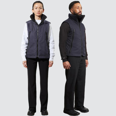 A man and a woman stand, each wearing a unisex navy blue vest
