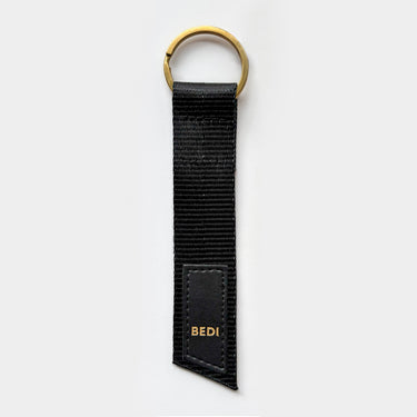 A simple keychain made from a black seatbelt, with gold brass ring and a faux leather logo patch with gold letters