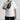 a man in a white tshirt wearing a green nylon cross body bag, against a plain grey background