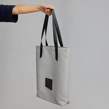 A model's arm holds a white tote bag with a black strap against a light grey background