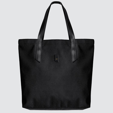 A black nylon tote bag with black medium-length straps and a black patch with gold logo text