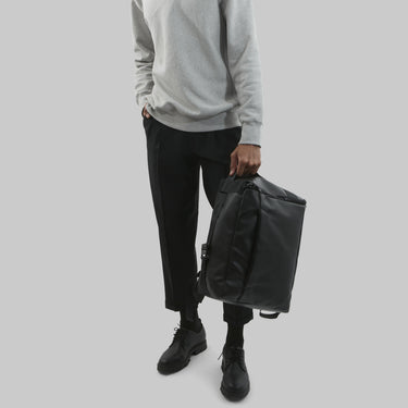 Person holding a black backpack against a plain background