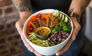 Tattooed man's hands holding a bowl with a variety of vegetables