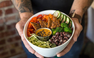 Tattooed man's hands holding a bowl with a variety of vegetables