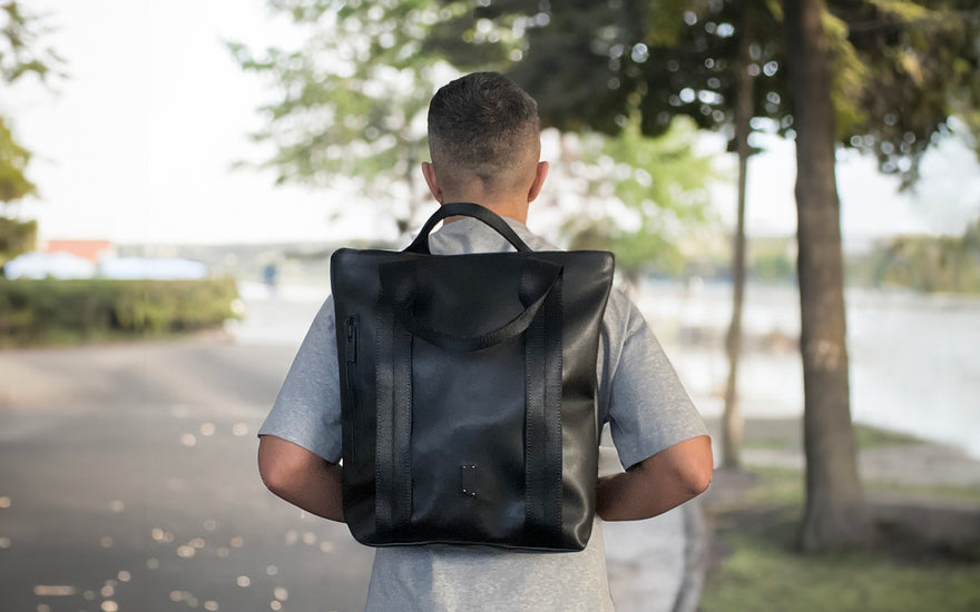 A man stands in a park wearing a totepack in backpack form