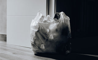 A plastic bag full of trash sits next to an open door. Black and white and stark lighting creates a moody vibe