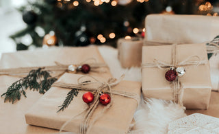 A pile of gifts wrapped in brown paper, with an out of focus christmas tree in the background