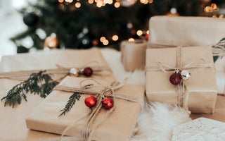 A pile of gifts wrapped in brown paper, with an out of focus christmas tree in the background