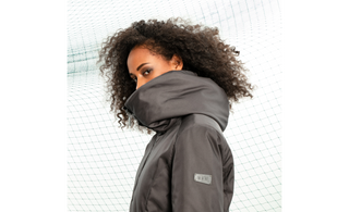 A female model burries the bottom part of her face in the high neck/hood of the Orsola coat, and looks sideways at the camaera