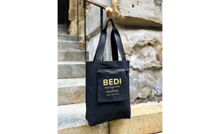 an image of the reversible tote bag displayed inside out showing off the inside pocket logo, pictured on outside stairs and a stone wall