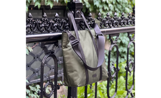 Image of an Evergreen utilitarian tote, resting on a fancy black park fence by its handles.