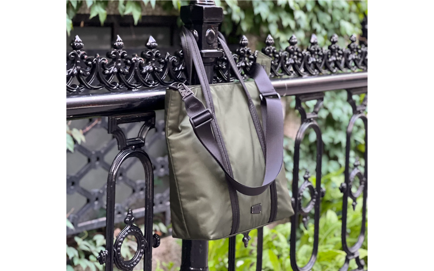 Image of an Evergreen utilitarian tote, resting on a fancy black park fence by its handles.