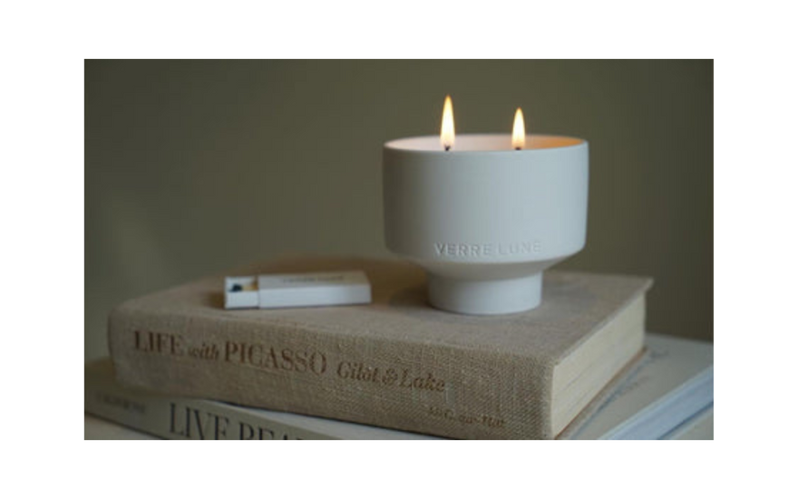 A lit candle with two flames sits on two books, with a lighter next to it