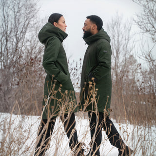 A man and a woman, both wearing green winter coats, walk toward each other in a snowy field