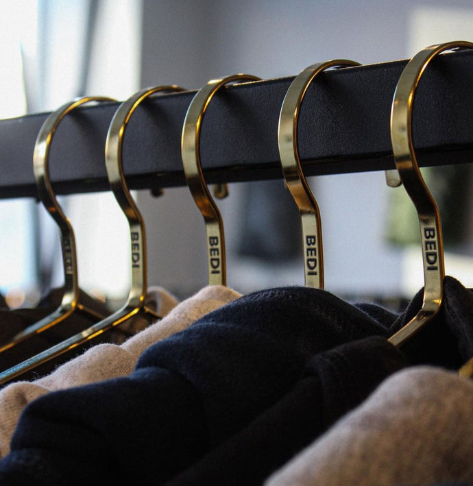 A row of five brass hangers with the Bedi logo embossed, hanging from a black metal rack