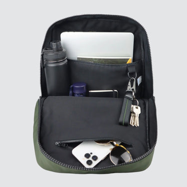 The CHE backpack with the main compartment open, showing the contents. Contents include: a water bottle, umbrella, magazine, laptop, iPhone, sunglasses and keychain. 