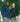 A male and female model stand in front of a leafy green tree, each wearing a sweater and a bag from Bedi