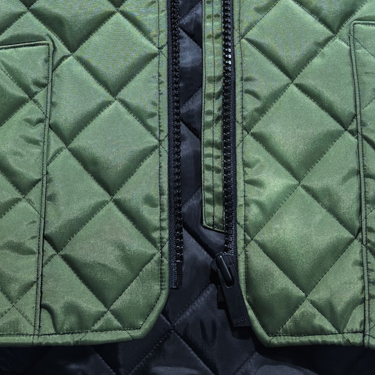 Close-up of a quilted jacket showing an olive green diamond-stitched exterior with black zippers and a dark inner lining.