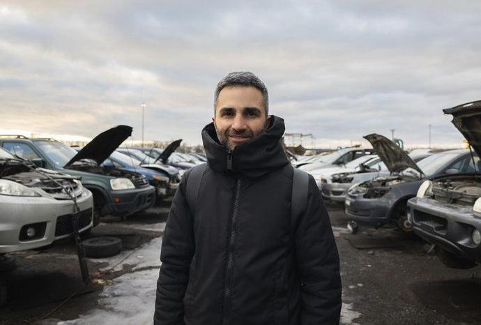 Founder Inder Bedi stands in a car scrapyard in winter, wearing the Ansel coat, and smiling at the camera
