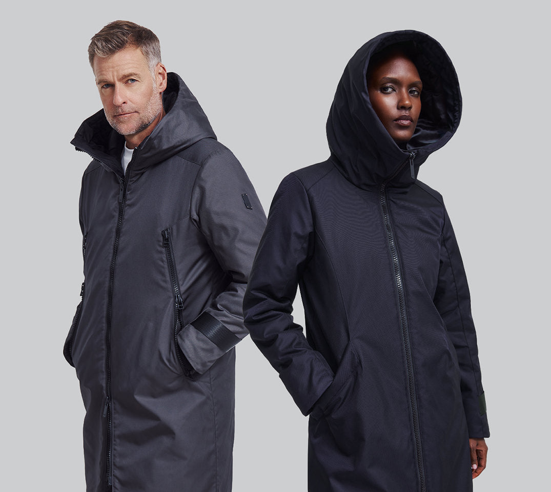 A male and a female model both wearing winter coats pose against a plain background