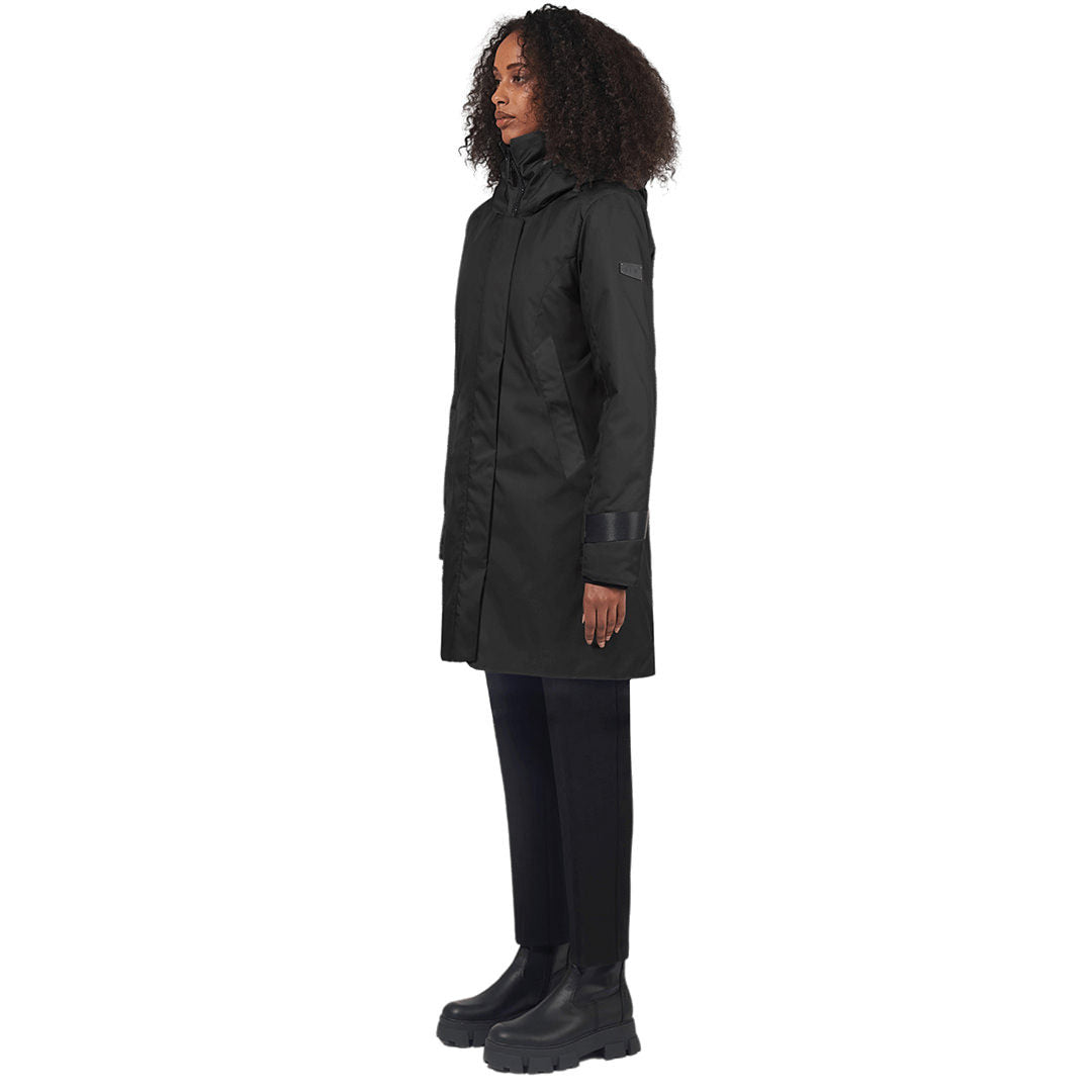 Female model stands to the side wearing a mid-thigh length black coat, against a white background