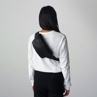 A black leather sling bag worn crossbody on a woman