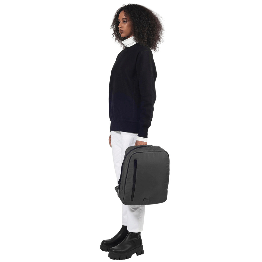 female stands side facing camera handhelding the che backpack in grey on a white background