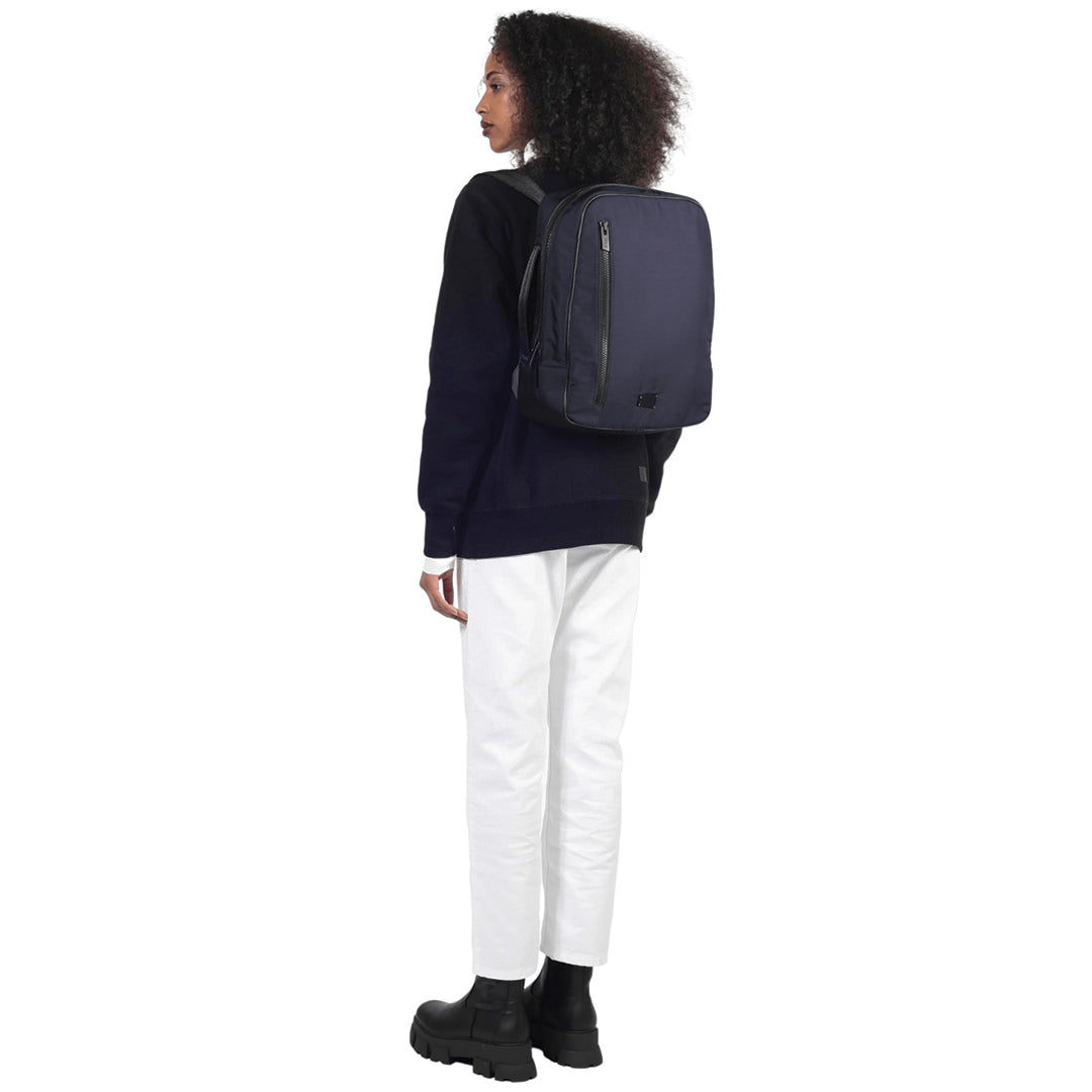 female stands back facing camera wearing the che backpack in navy on a white background