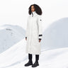 A woman standing in a long white winter coat with a snowy background