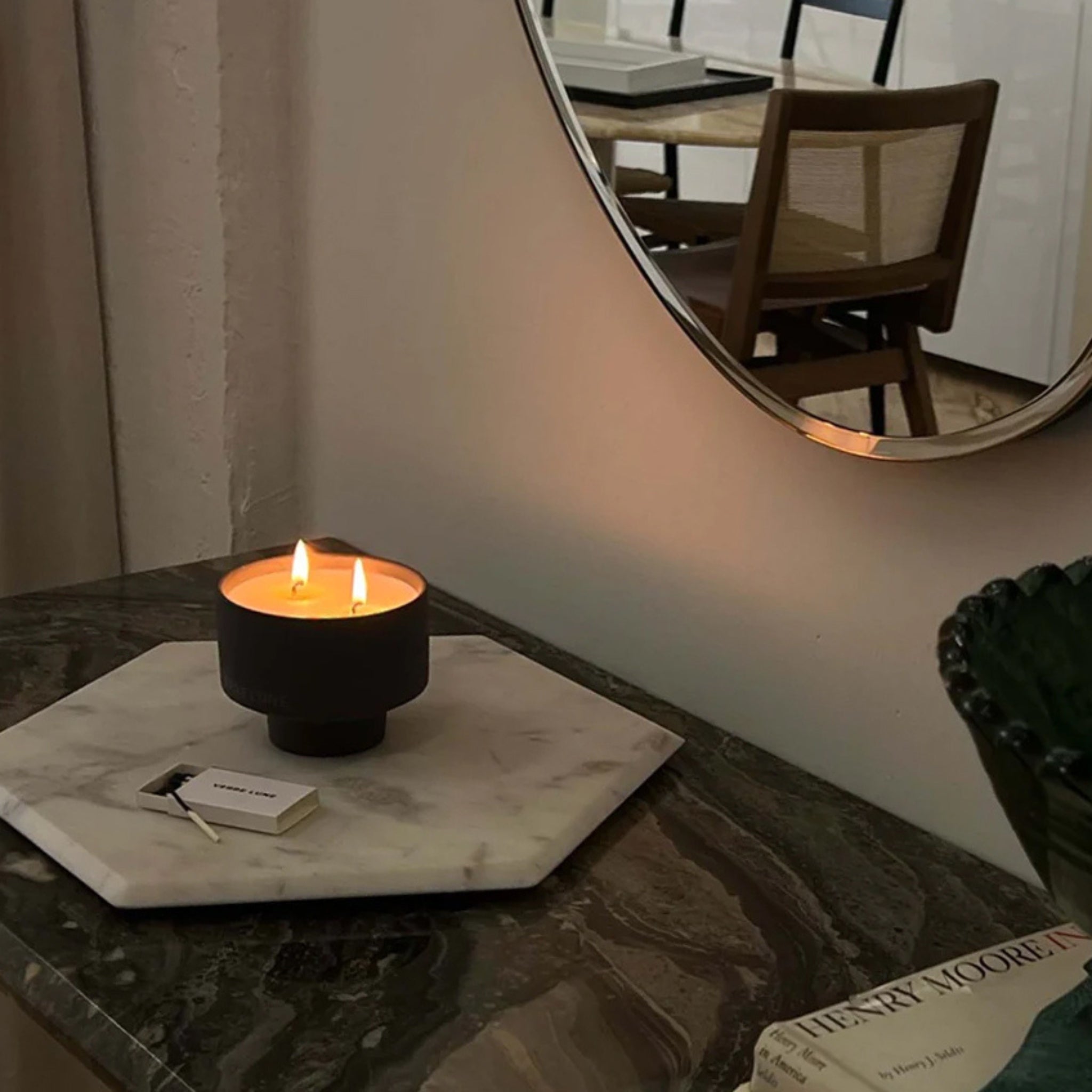 a candle lit with verre lune branded matches by its side in a modern dining room setting