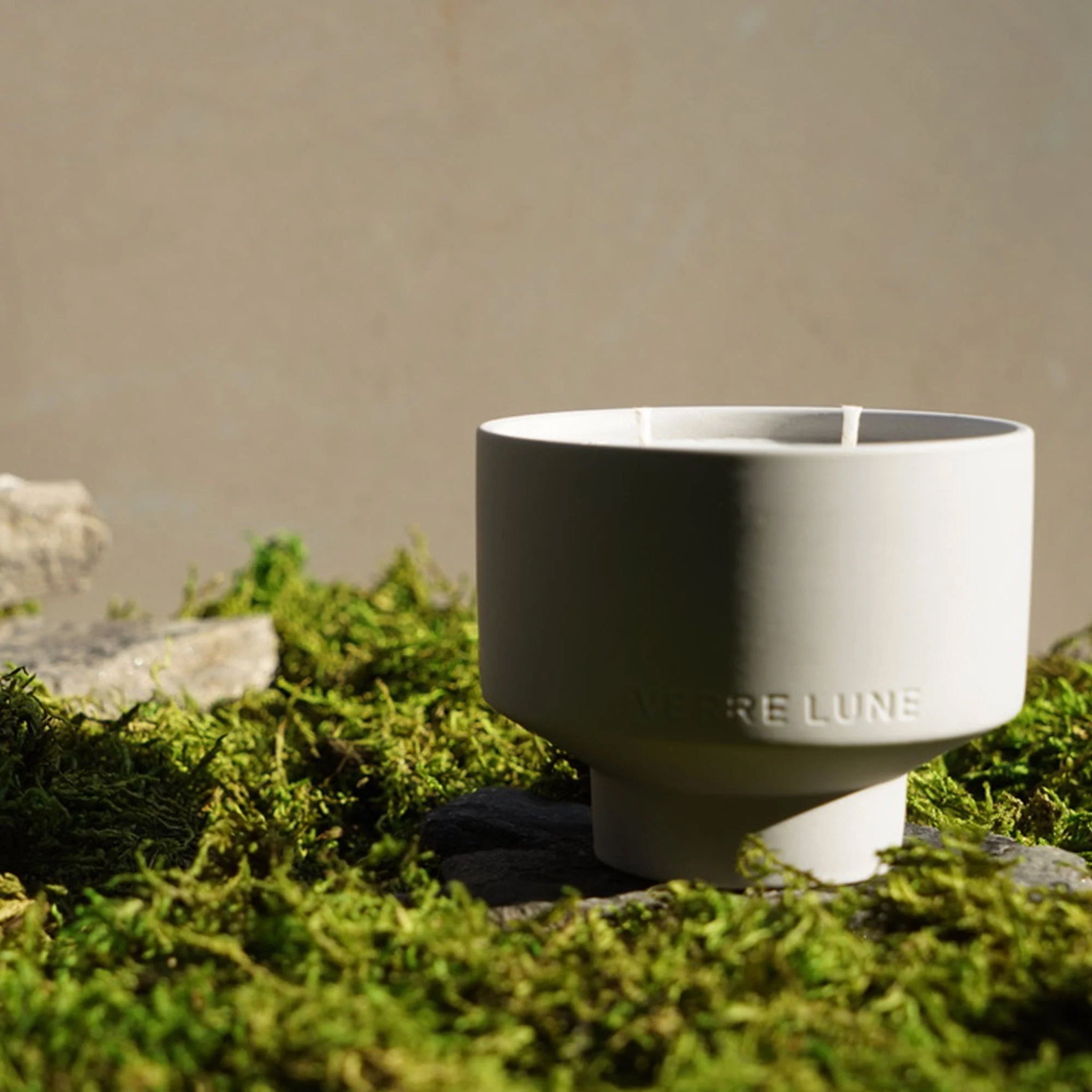 Verre Lune stone candle in the middle of a scene in nature with moss and rocks.