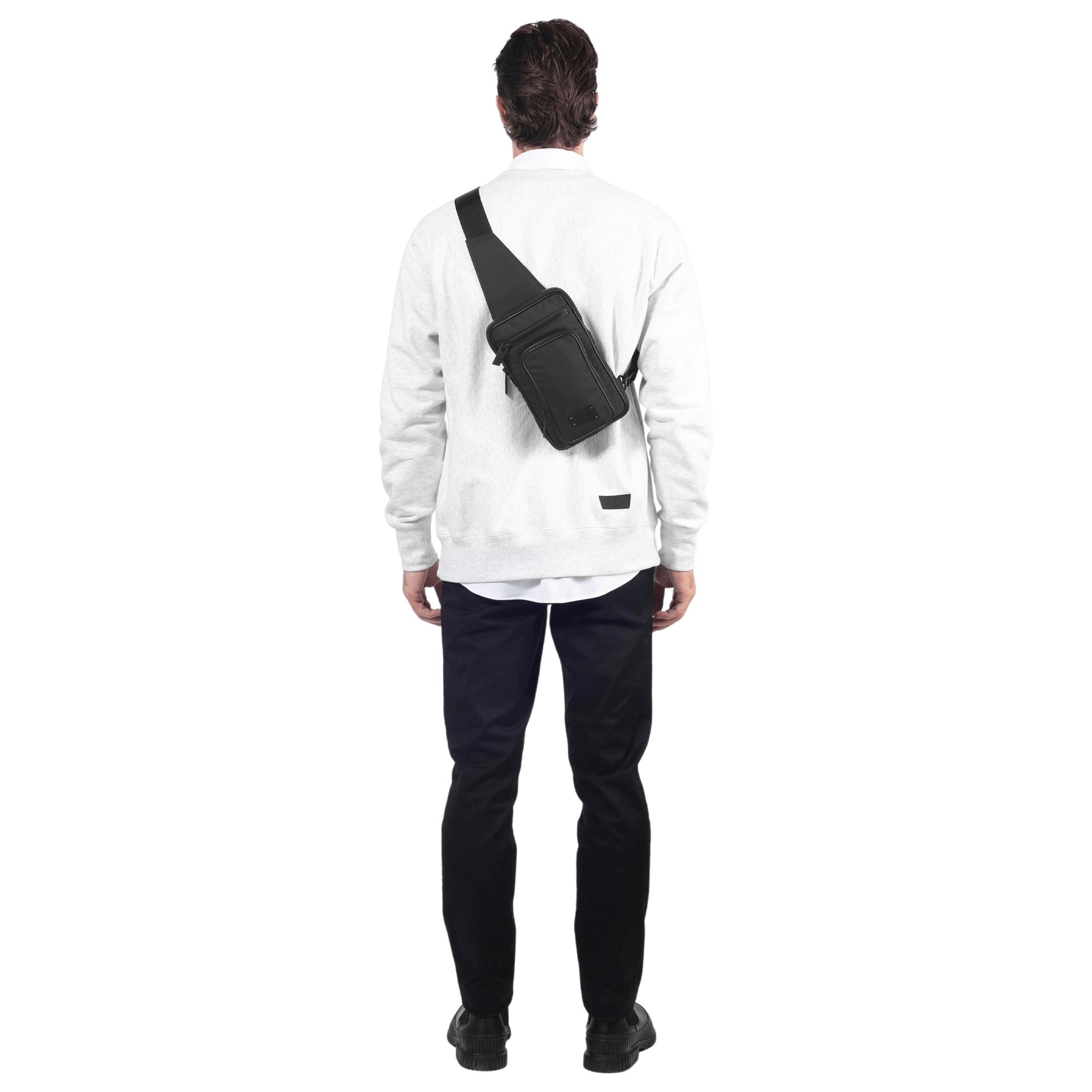 male stands with a black sling worn crossbody style on his back on a white background