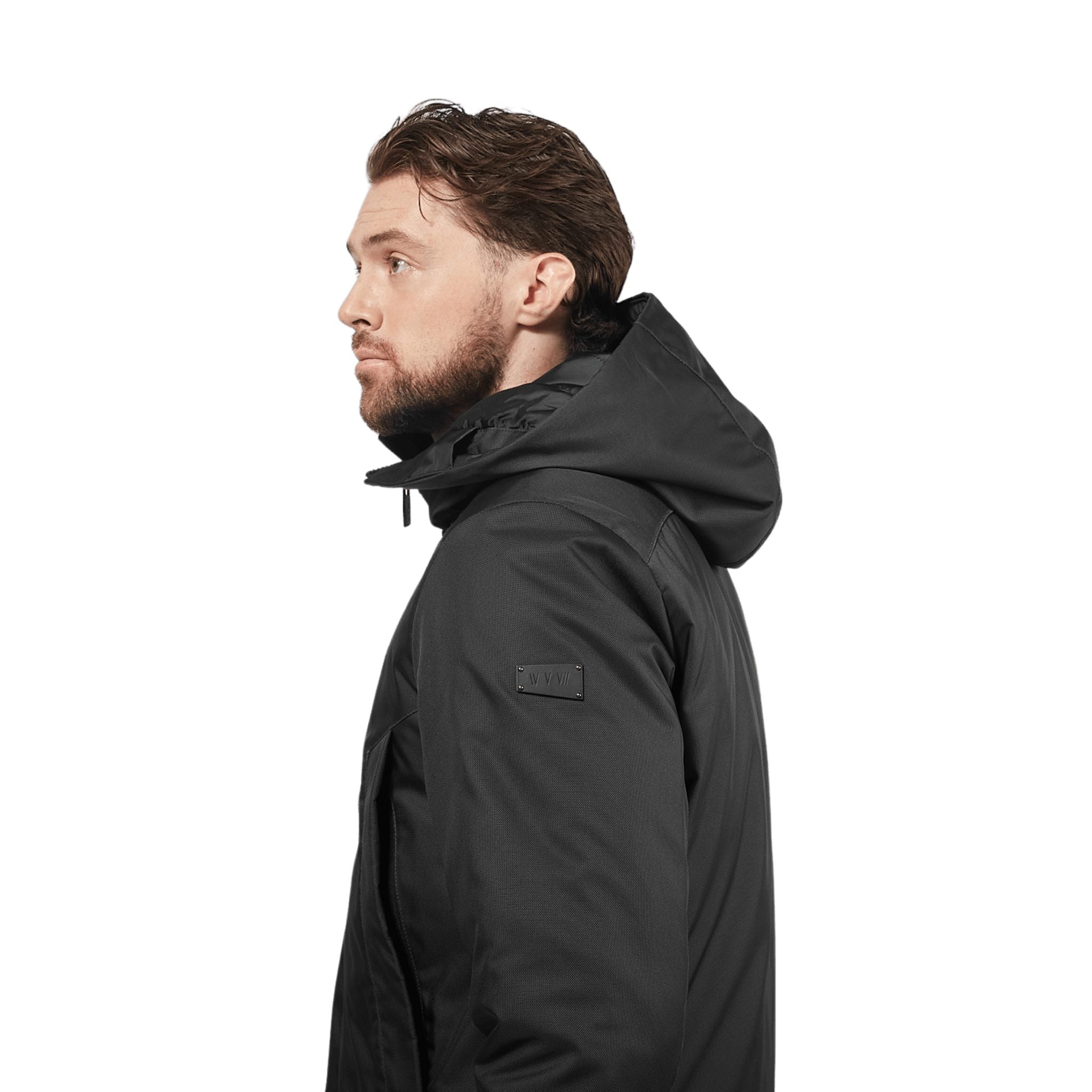 male model stands, the camera is closing up on the side details of the jacket, wearing a black utilitarian style waist length jacket on a white background.