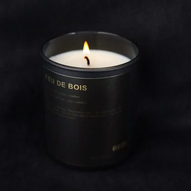 Candle in a black container labeled 'Feu de Bois' on a dark background