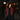 A woman stands outdoors at night in front of a storefront window, wearing a quilted burgundy jacket over a black top and dark jeans. A lit street lamp and the shop interior are visible in the background.