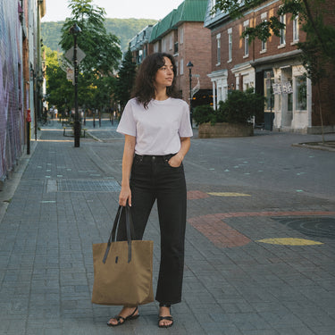Woman walking down a street holding a brown tote bag