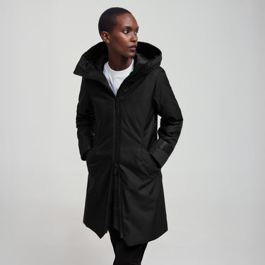 A woman wearing a black 3/4 length coat with the bottom zip unzipped