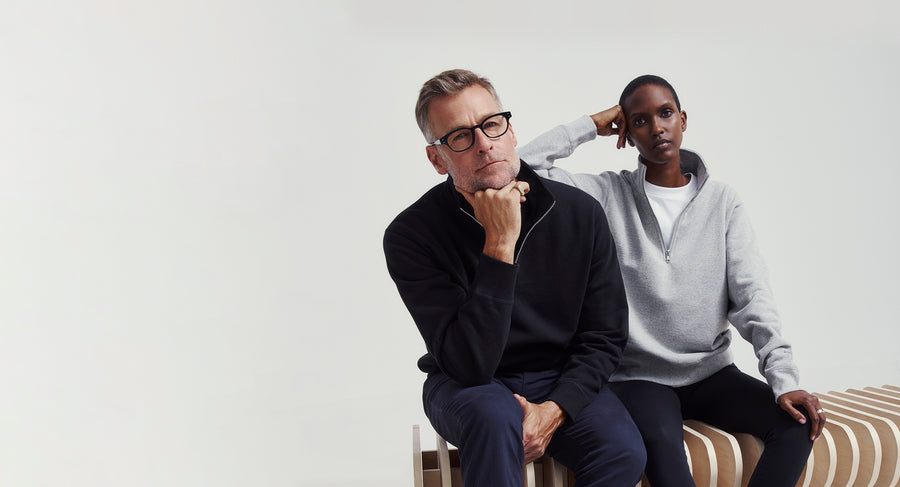 Two people wearing 1/4 zip sweaters sitting on a white background