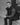 Man sitting on steps wearing a dark vest and pants in a black and white photo.