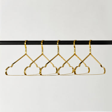 Four gold metal clothes hangers hanging from a black rod against a light grey background.