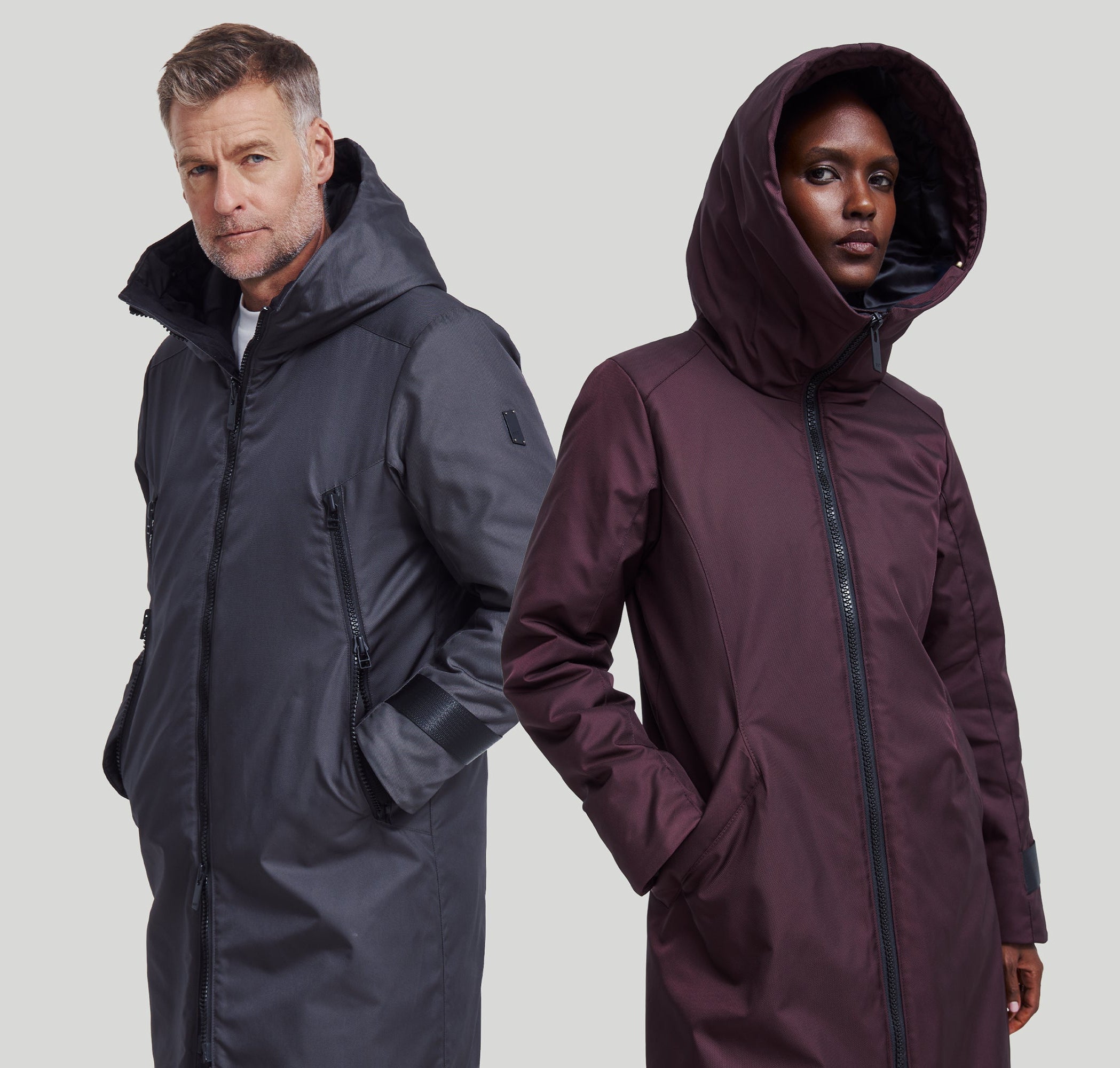 A male and a female model both wearing winter coats pose against a plain background