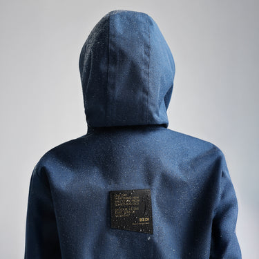 back view of a navy raincoat with raindrops beading on the fabric