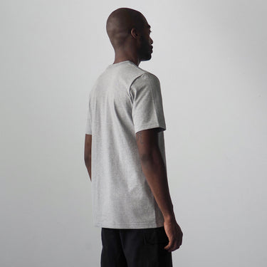 A man shown from the back wearing a light gray short-sleeve crewneck t-shirt and black pants, standing against a plain light gray studio background.