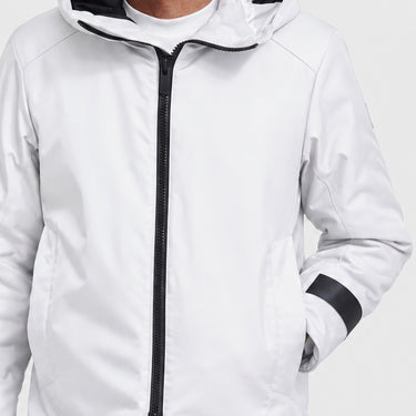 A close-up of a person wearing a white hooded jacket with a black front zipper and black sleeve accent, photographed against a light gray studio background.